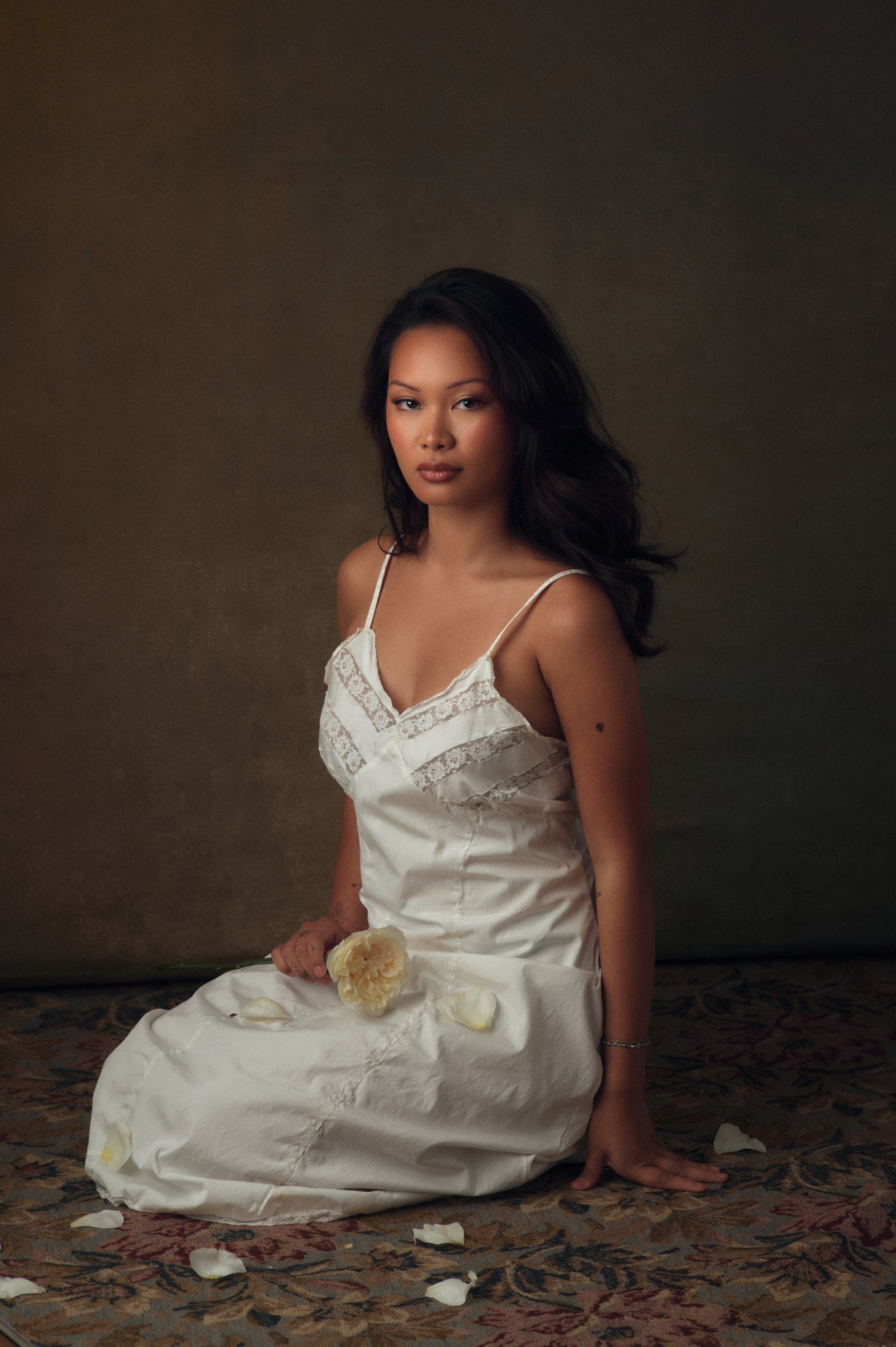 Editorial bridal portrait — white slip dress, a rose held to the face, painterly studio backdrop