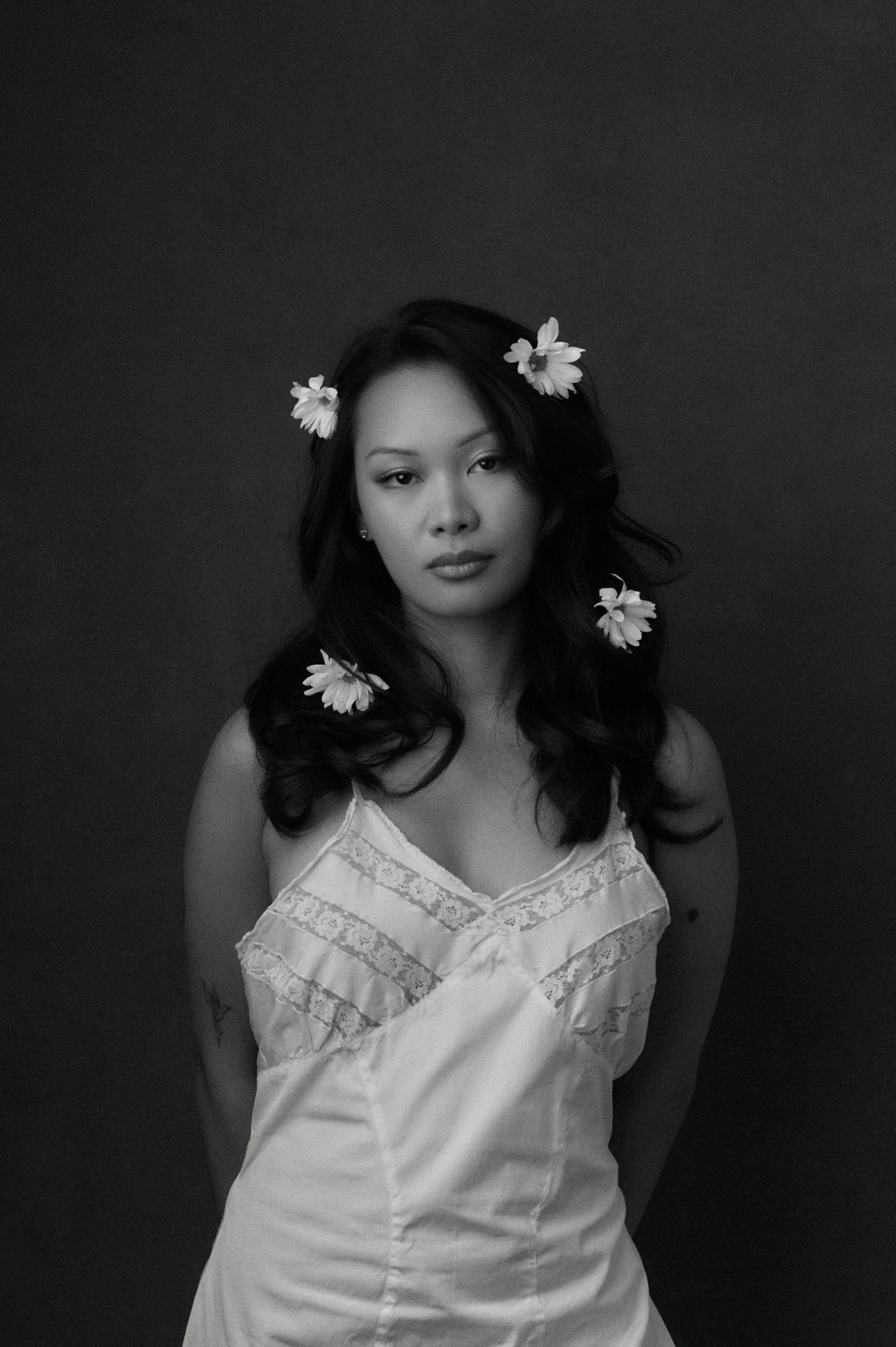 Black-and-white editorial portrait, flowers in the hair against a dark backdrop