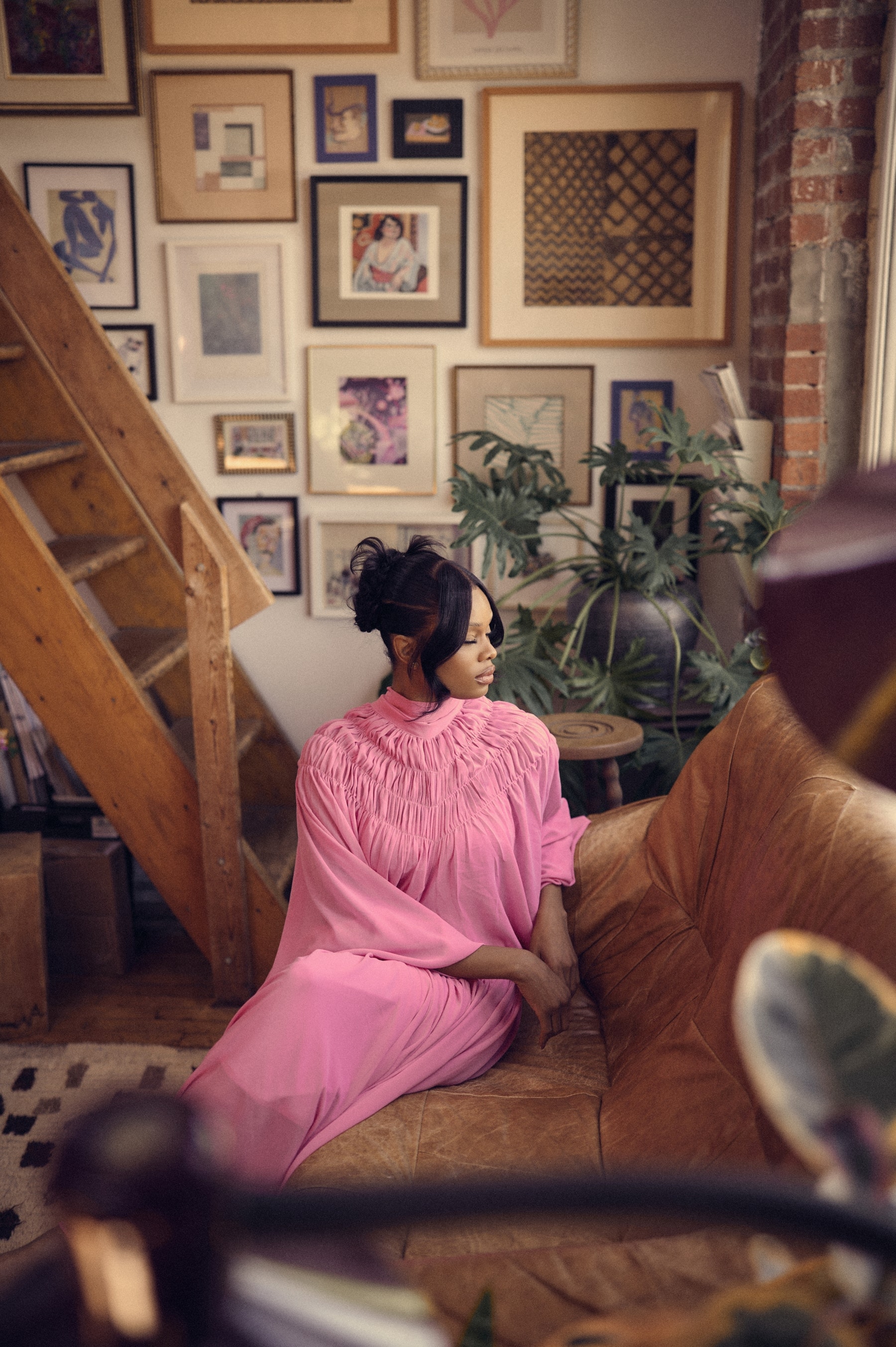 Editorial portrait in a flowing pink gown on a leather sofa, art-filled loft