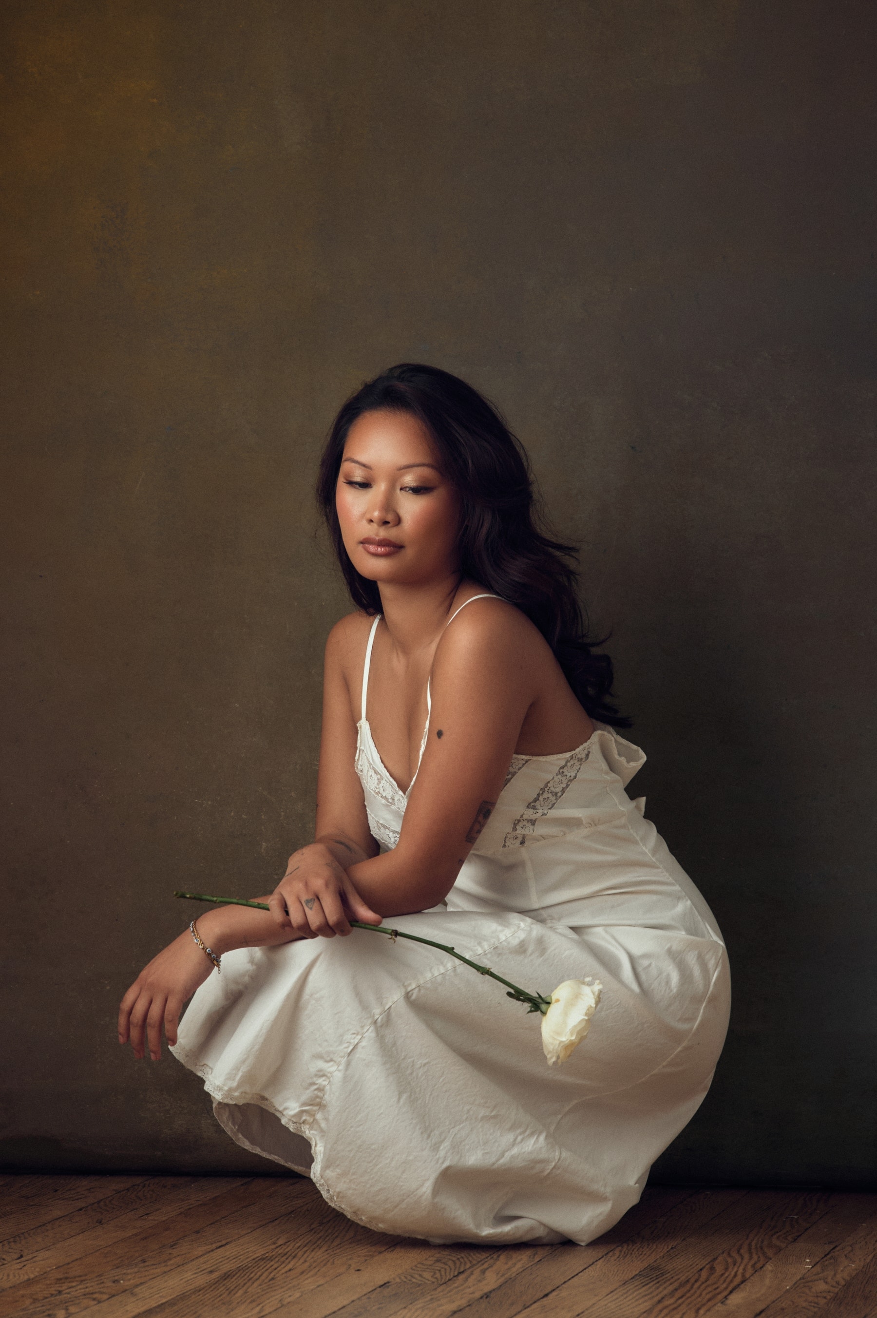 Editorial portrait seated in a white slip dress holding a rose