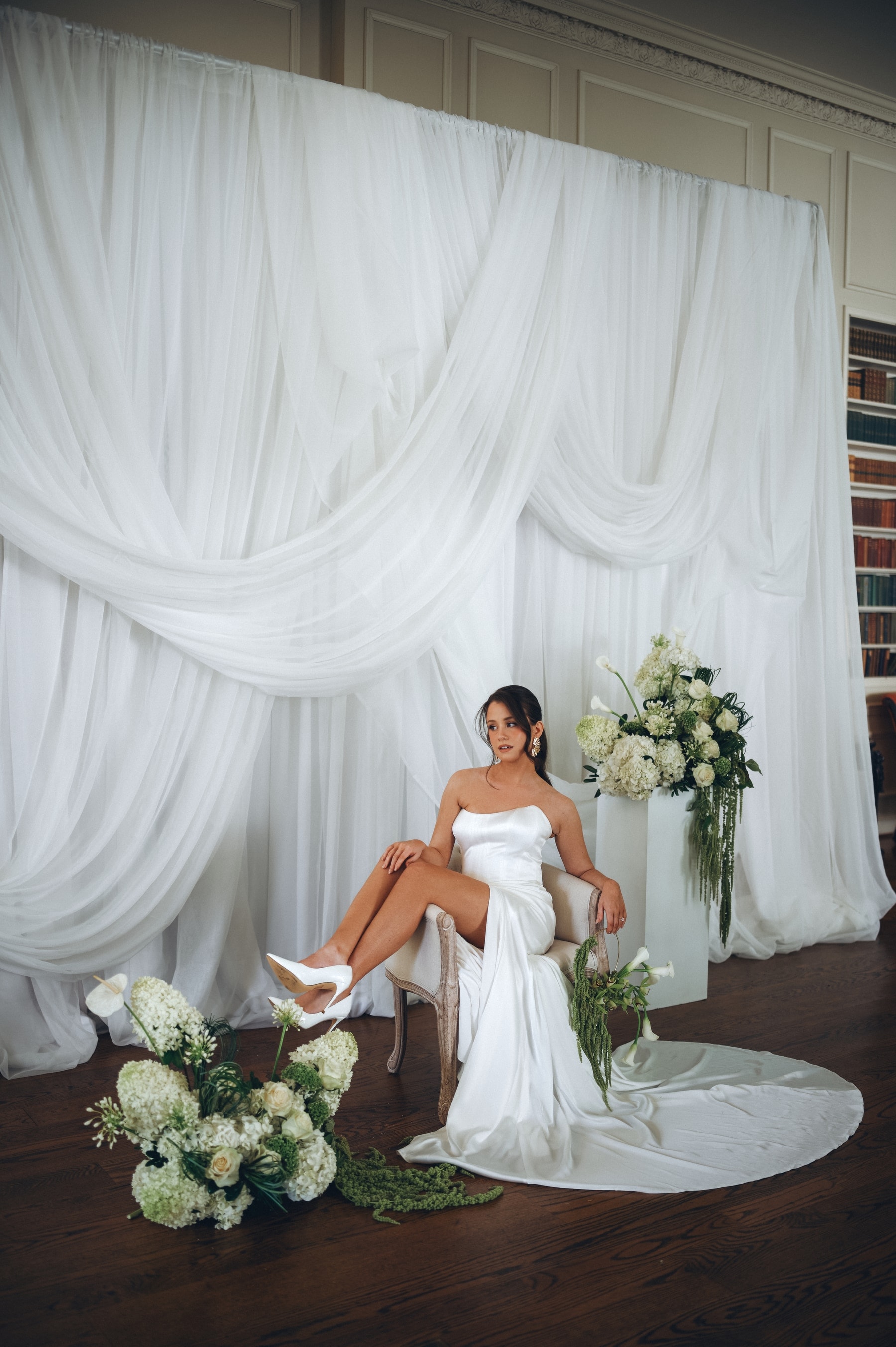 Editorial bridal portrait in the studio — satin gown and heels against draped white tulle