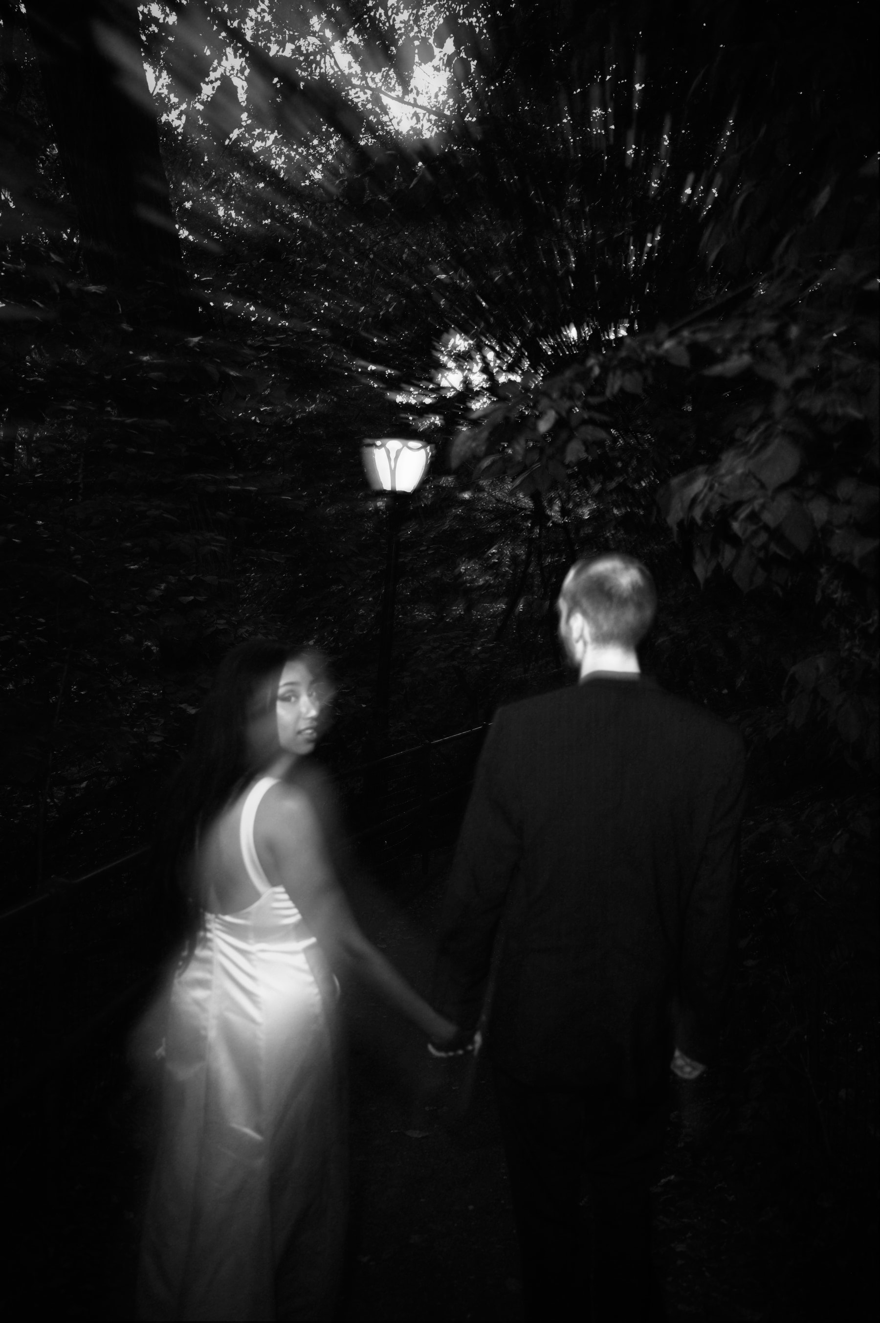 June looking back on a lamplit Central Park path after dark, motion in her dress, black and white