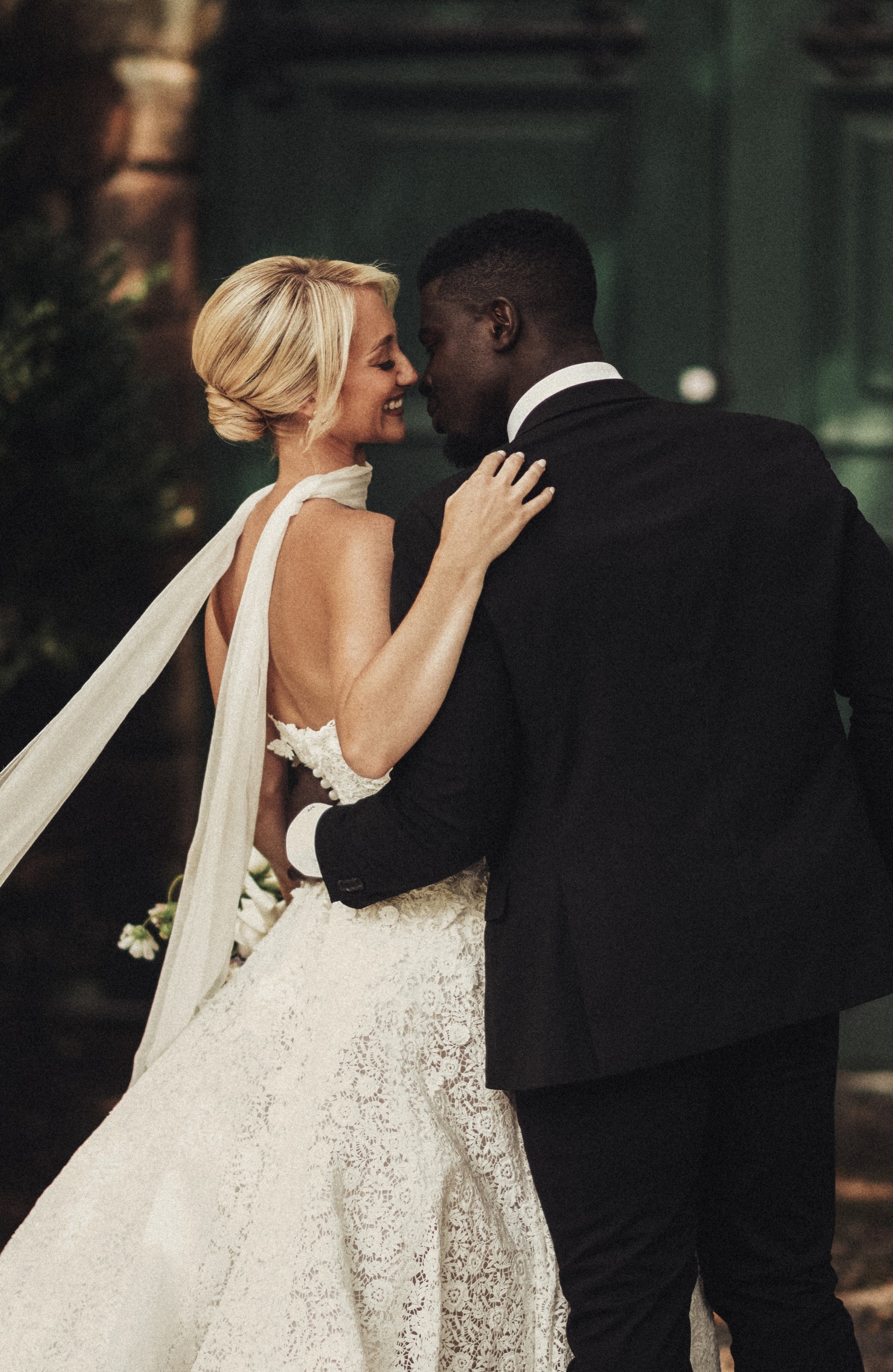 Bride and groom embracing outside deep-green doors, veil trailing over a lace gown