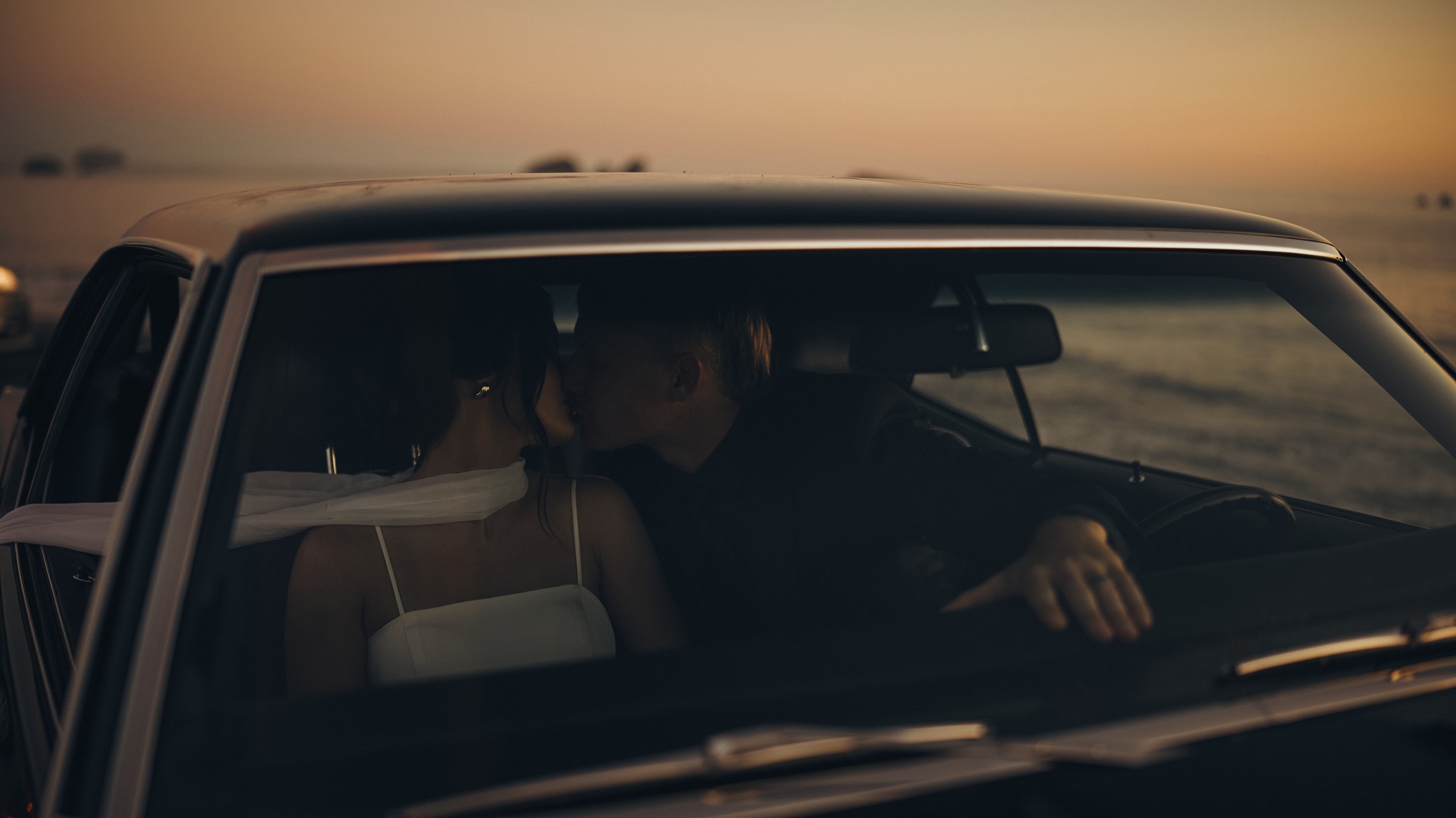 Bride and groom kissing inside a vintage car by the sea, black and white