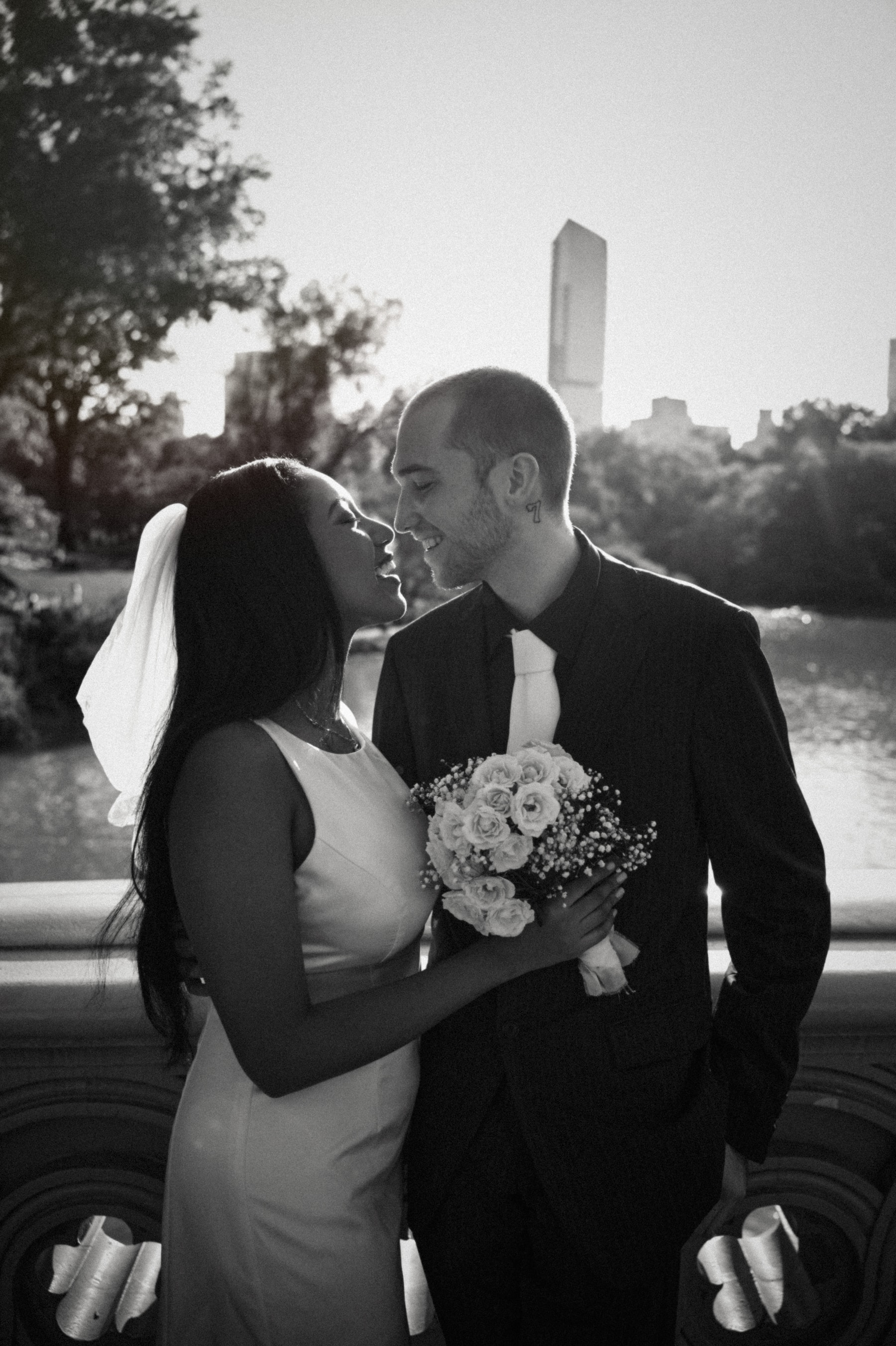 June and Elias kissing on Bow Bridge with the New York City skyline behind them, black and white
