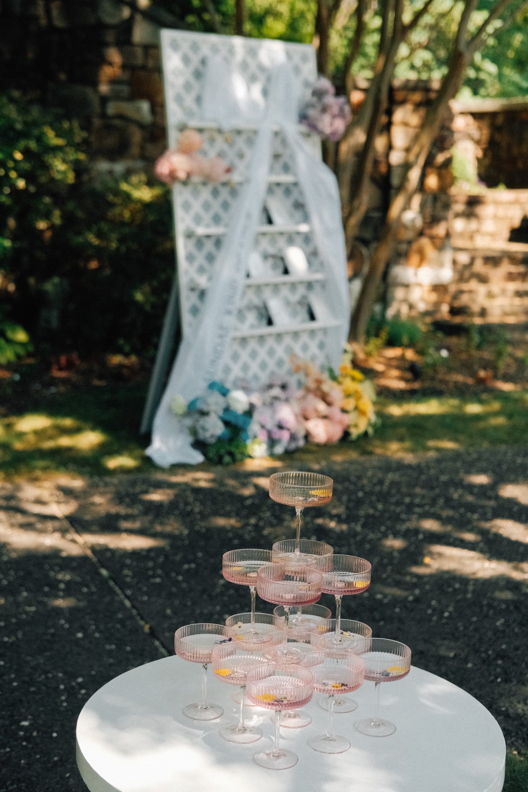 Champagne coupe tower in the garden, pastel florals softening the background